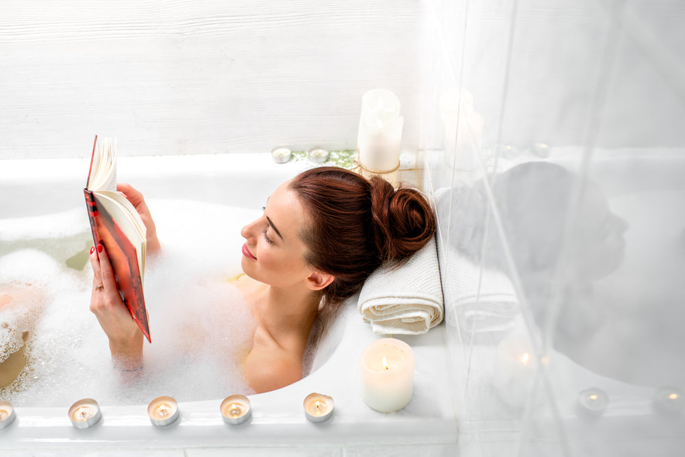 Spa accessories and candles on bathtub filled with foam and rose